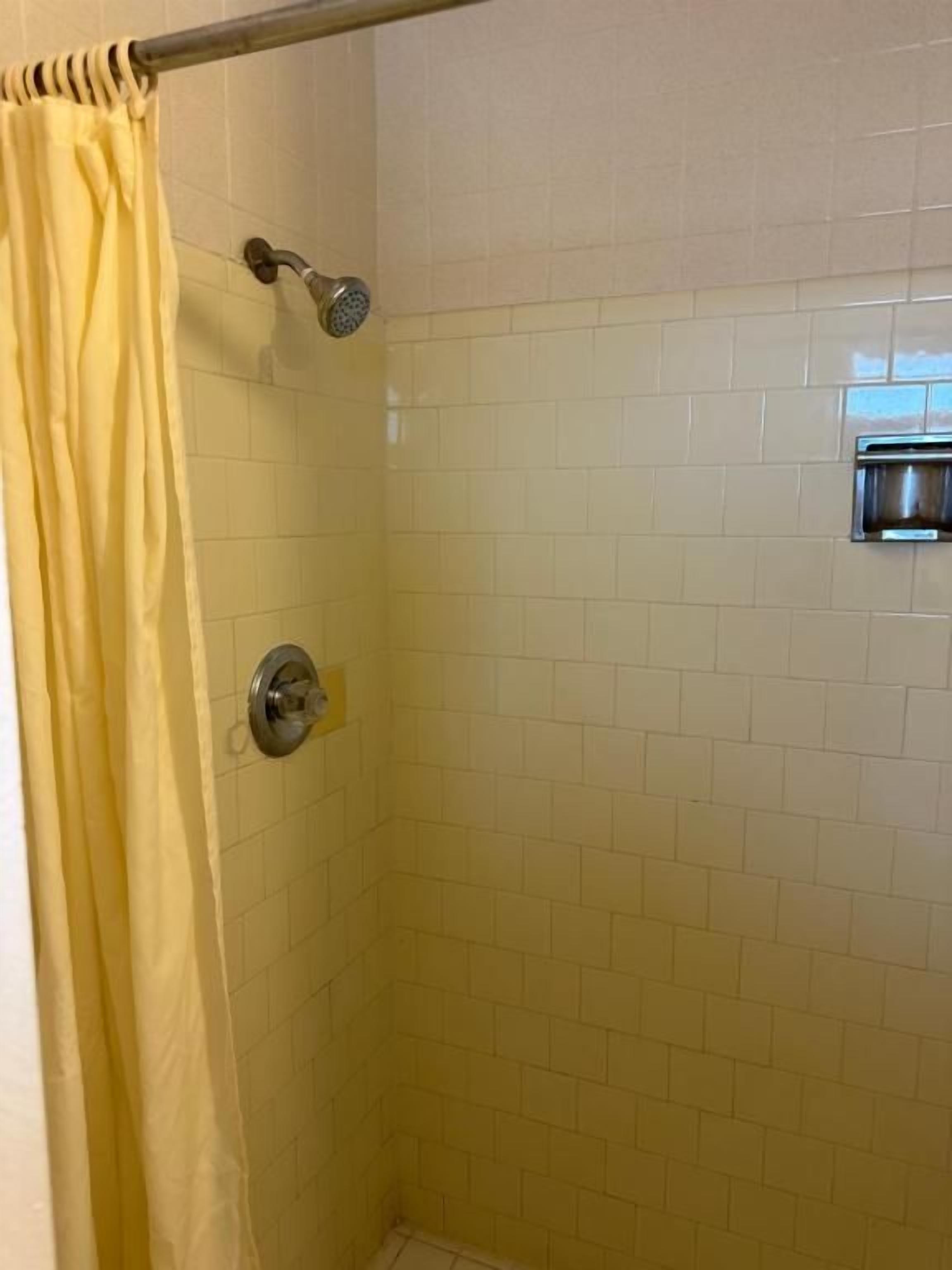 A shower with a yellow curtain, a handheld showerhead, and a wall-mounted faucet.