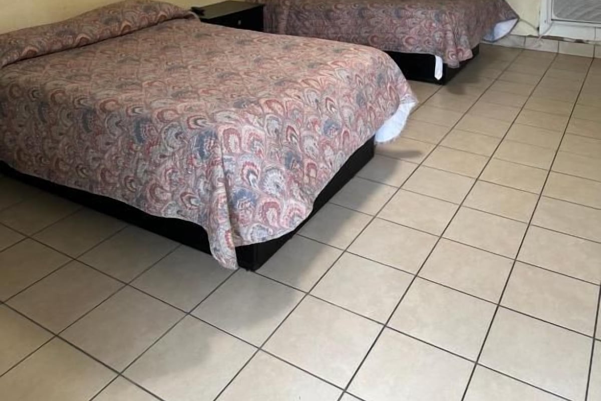 A room with two beds, a ceiling light, and a tiled floor.