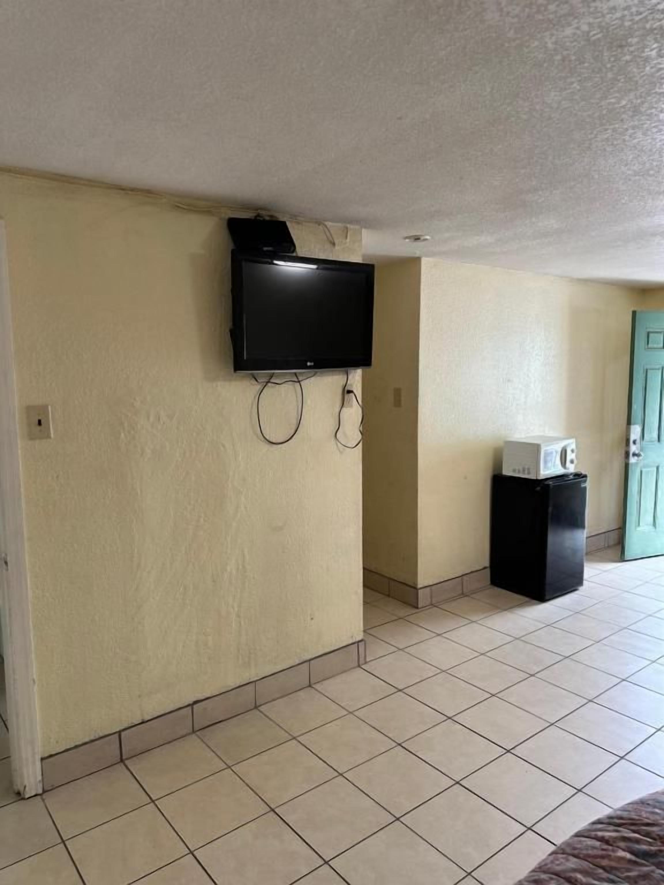 A room with a flat-screen TV mounted on the wall, a small black speaker, and a white microwave on a black stand.