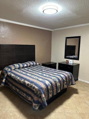 A bedroom with a bed, a nightstand, a dresser, a mirror, and a ceiling light. - Sands Motel (San Antonio)