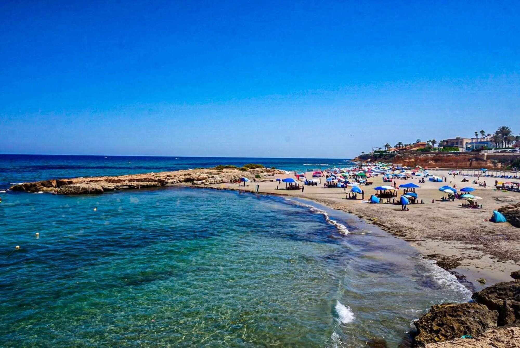 Une plage avec une eau claire, un rivage rocheux et des parasols.