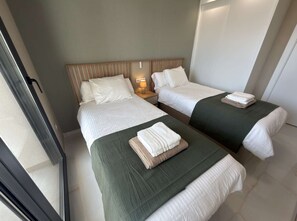 A hotel room with two beds, each with a green bedspread and white linens. There is a nightstand with a lamp between the beds. - Modern Luxury Penthouse with Private Rooftop Terrace & Pool Access (Los Almendros)
