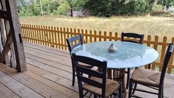 An outdoor wooden deck with a round glass table and four chairs, surrounded by a yellow picket fence.