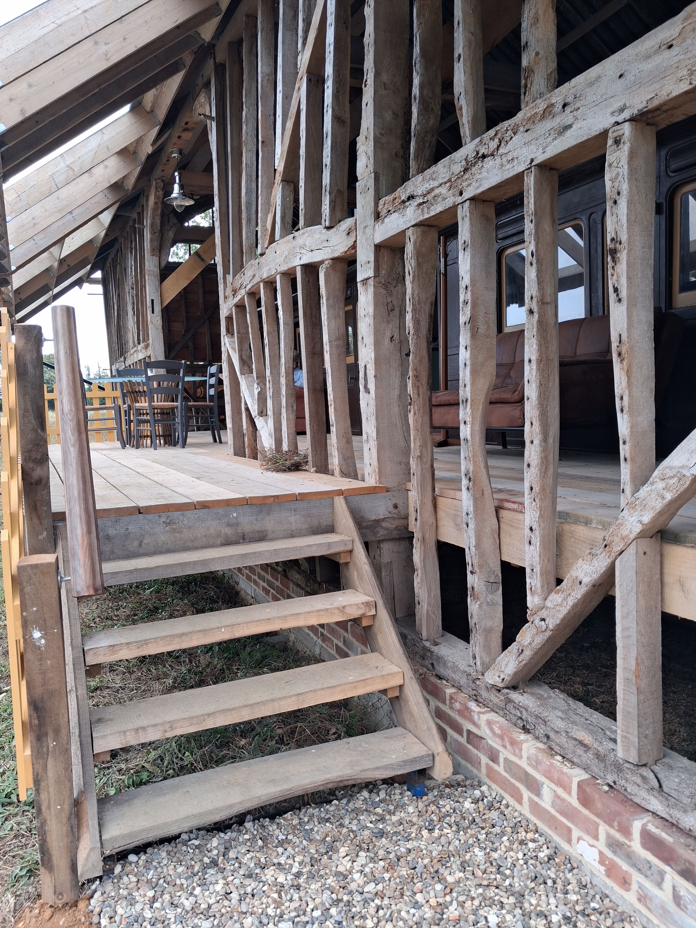 Een houten trap die leidt naar een overdekt terras met een bakstenen muur en een houten terras.