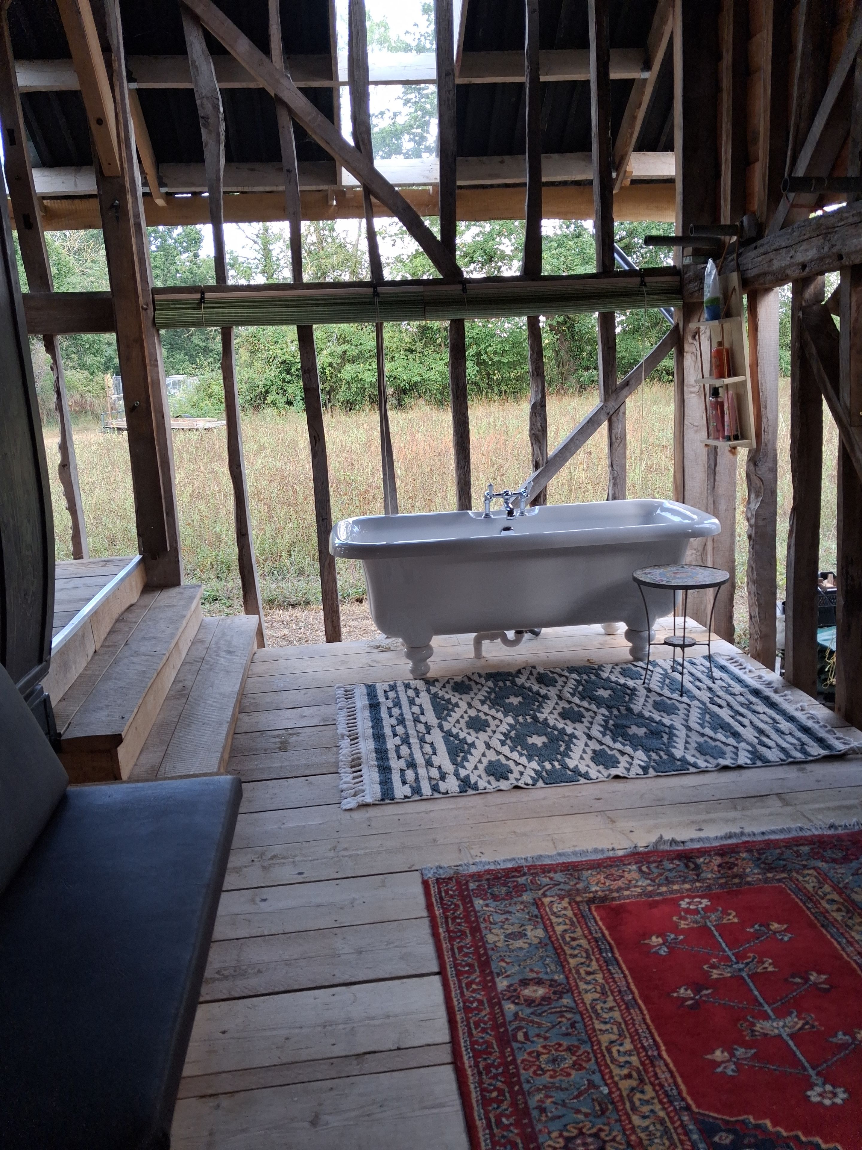 Une terrasse en bois rustique avec une baignoire, un tapis à motifs et un banc.
