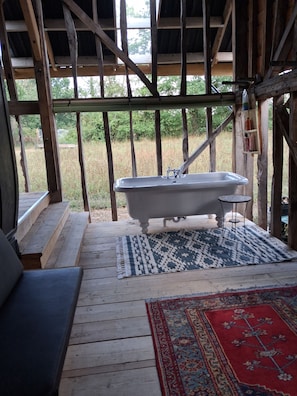 Une terrasse en bois rustique avec une baignoire, un tapis à motifs et un banc.