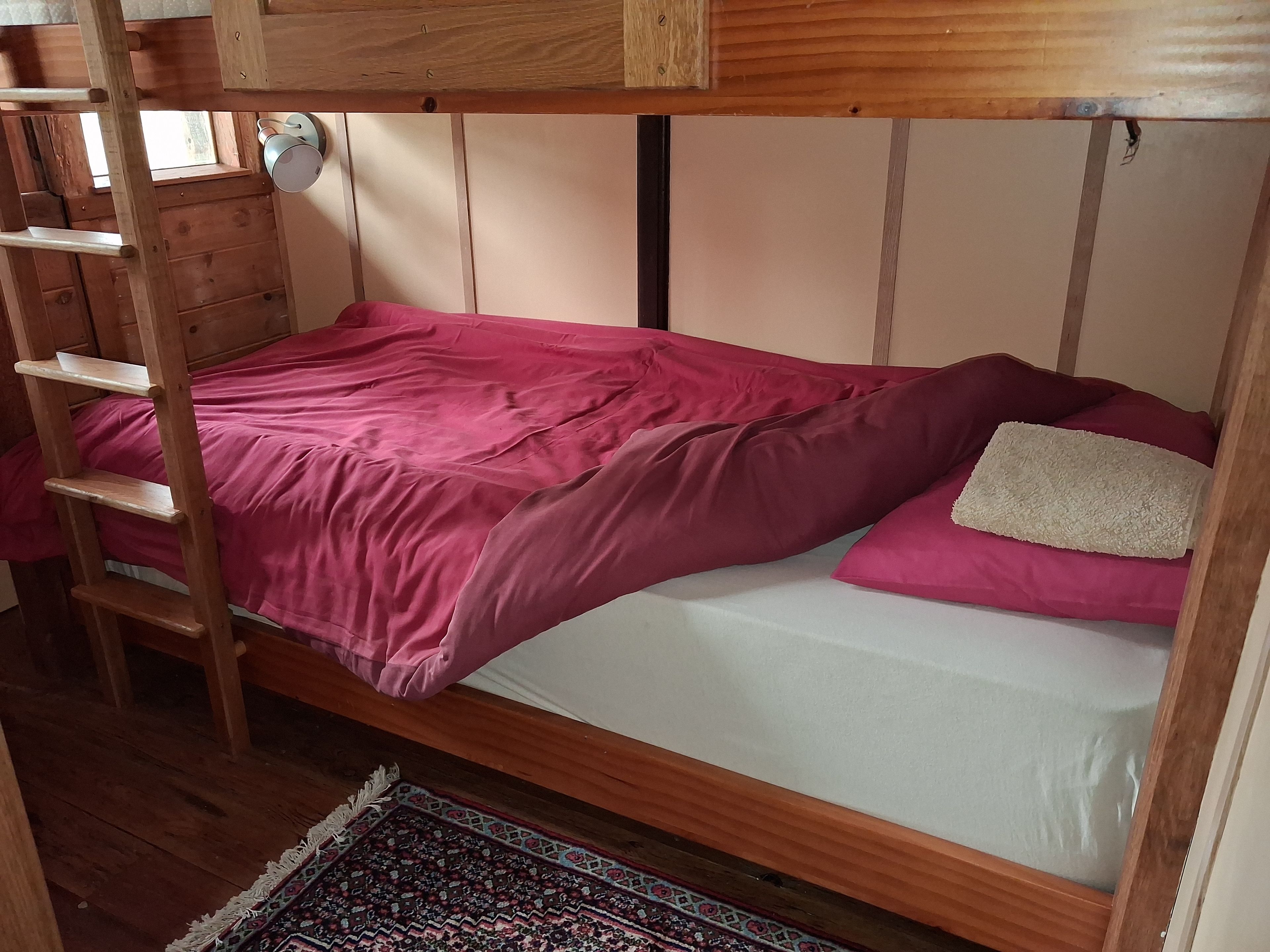 Un lit superposé avec une échelle en bois, une couvre-lit rose et un oreiller blanc.