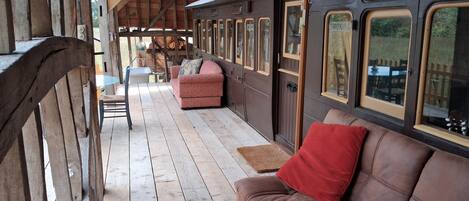 A covered outdoor seating area with a wooden bench, a cushioned sofa, and a wooden table.