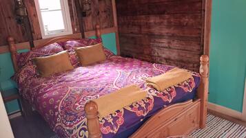 A wooden bed with a patterned bedspread and two pillows, a small round rug, and a window with a view of the outside.