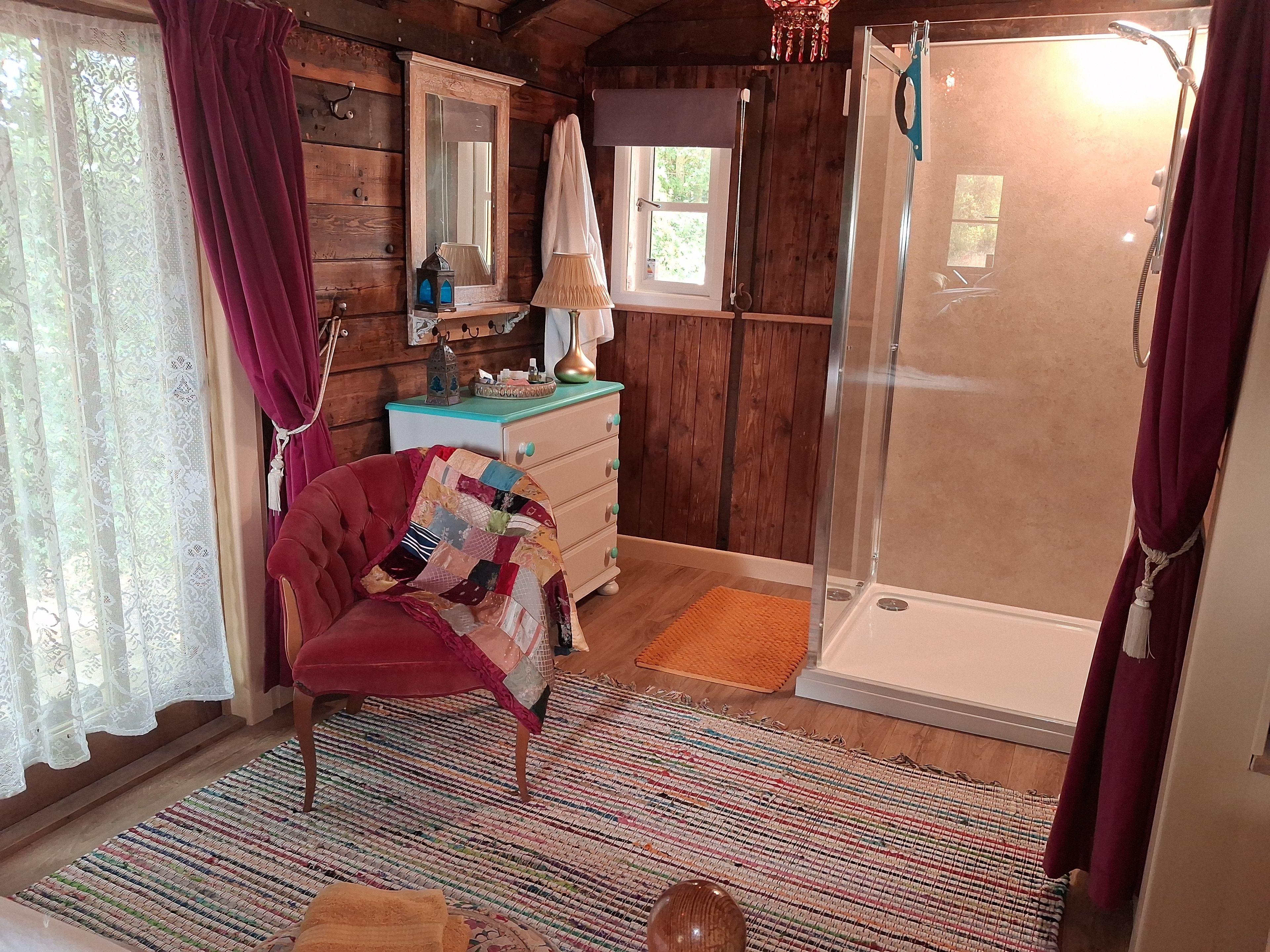 L’intérieur d’une cabane en bois, avec une chaise rouge, une commode, un miroir et un espace douche.