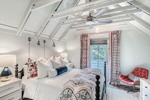 Ein Schlafzimmer mit einem Bett, Nachttischen, einem roten Sessel und einem Fenster mit Vorhängen.