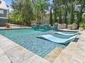 Ein Pool mit gewelltem Rand, umgeben von einer Steinterrasse und Kübelpflanzen.