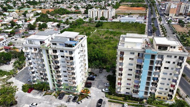 Un edificio residencial de gran altura con varios balcones, un estacionamiento y vistas del barrio circundante.