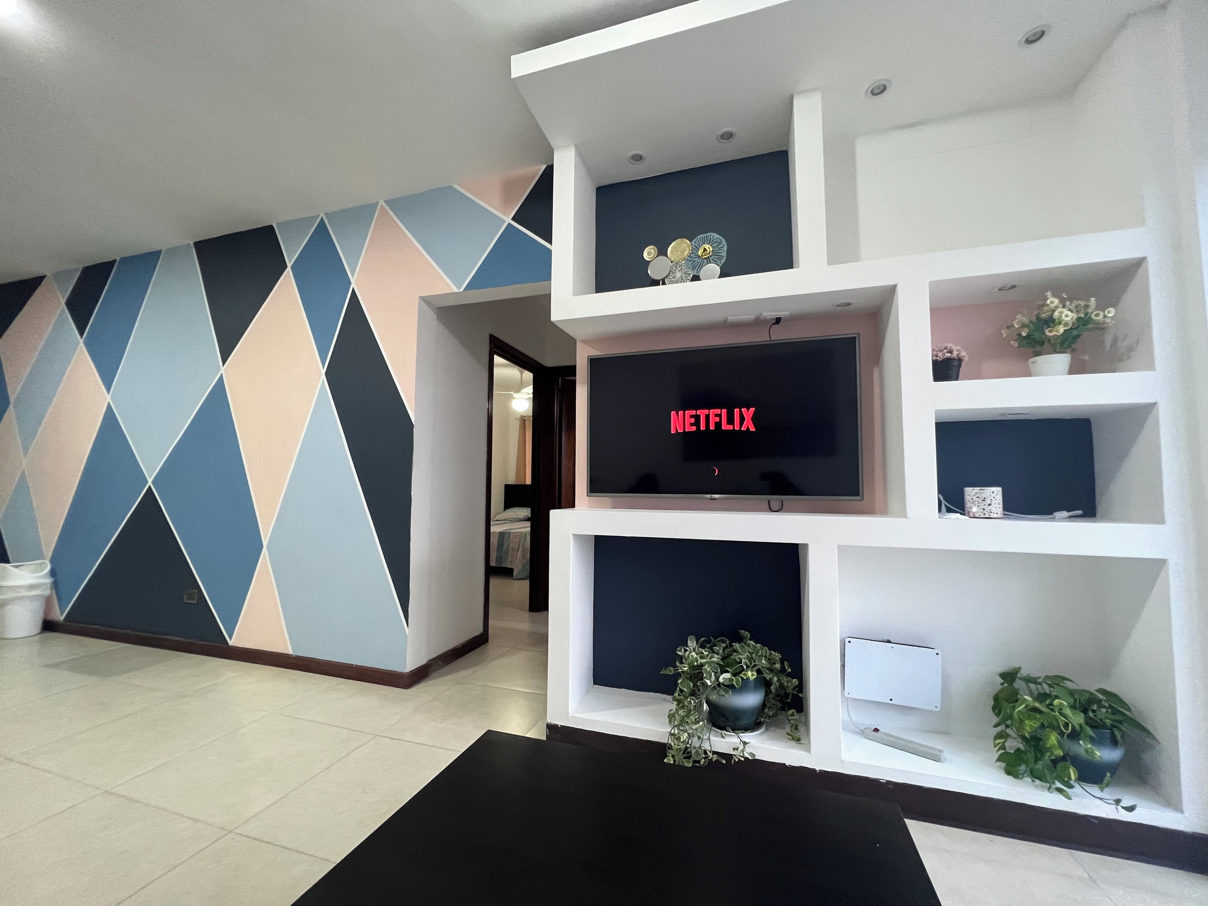 A modern living room with a flat-screen TV, a geometric-patterned wall, and built-in shelves with decorative items.