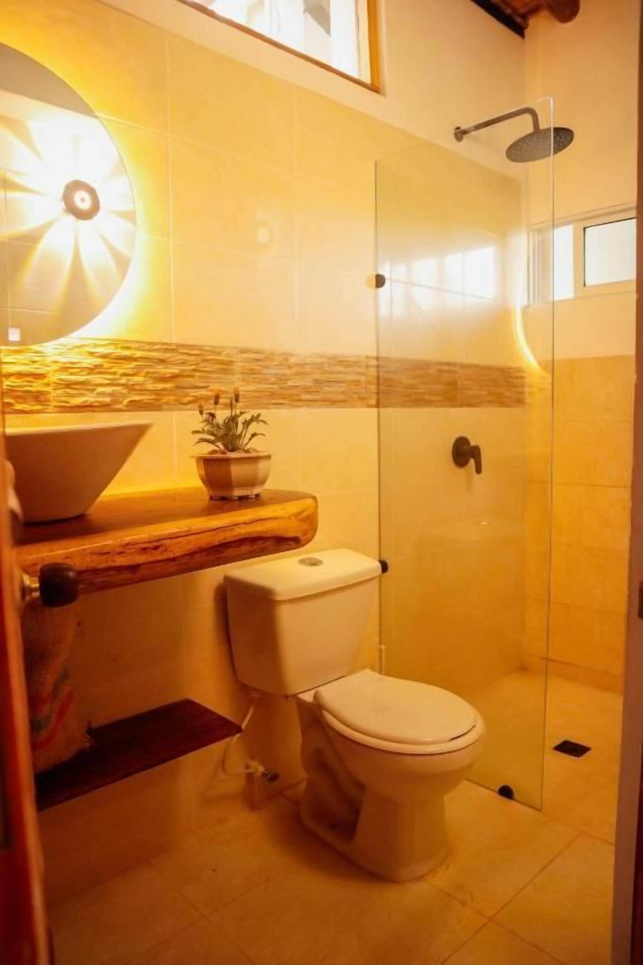 A bathroom with a toilet, a sink, a shower, and a wall-mounted light fixture.