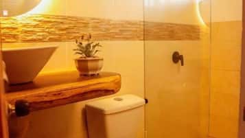 A bathroom with a toilet, a sink, a shower, and a wall-mounted light fixture.