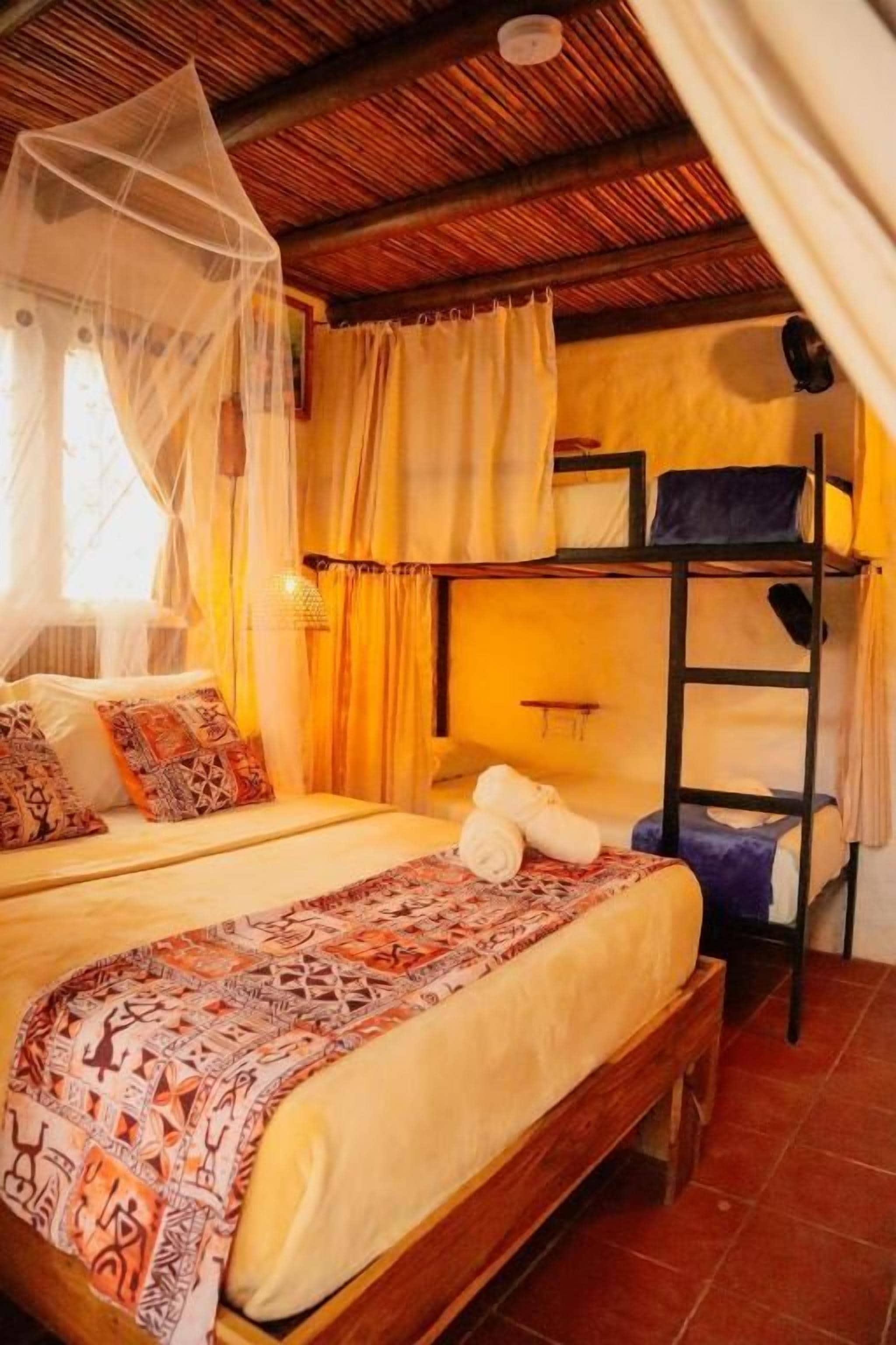 Quarto com cama, beliche, mosquiteiro e janela com cortinas.