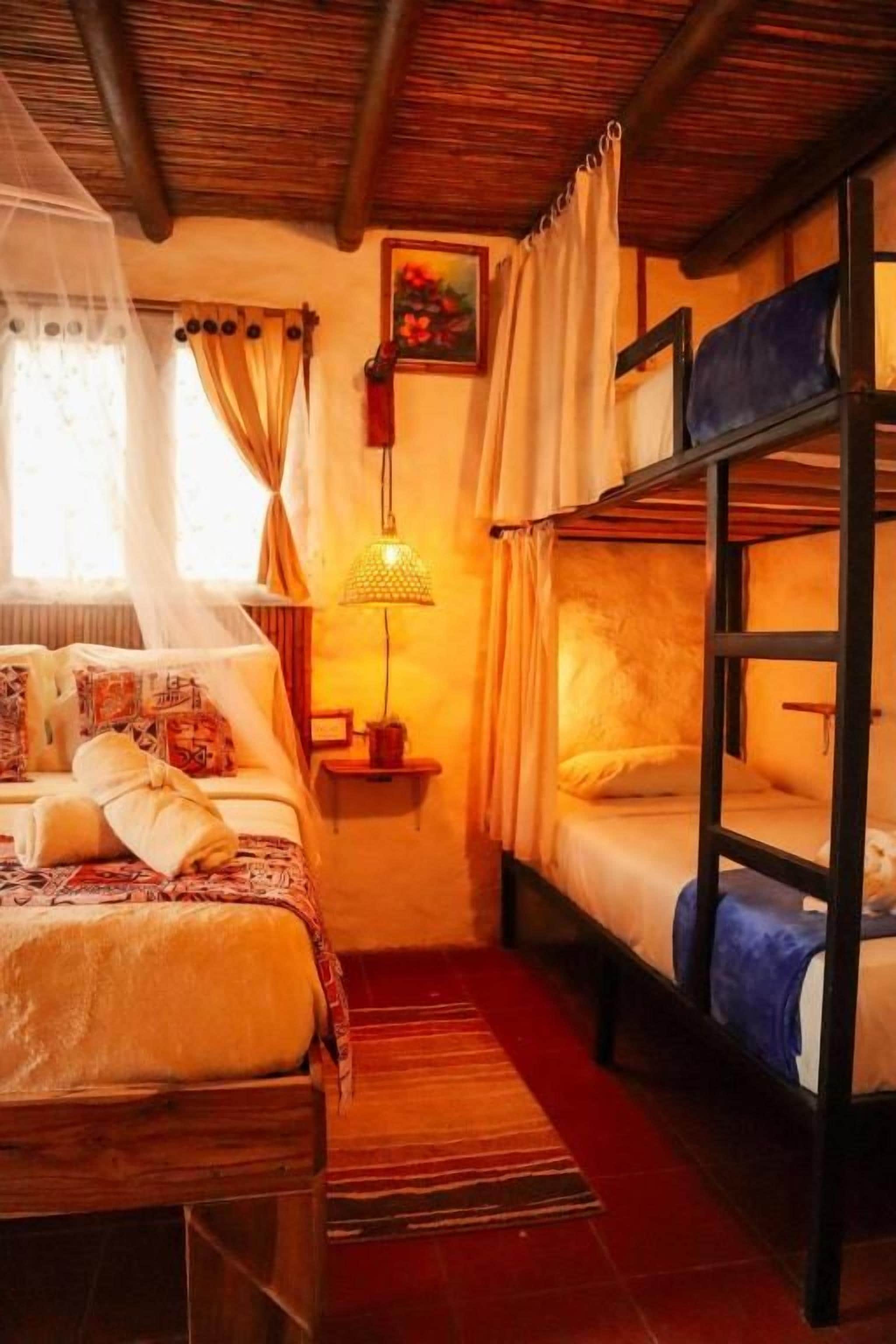 Quarto com beliches, mesa de cabeceira com abajur e janela com cortinas.