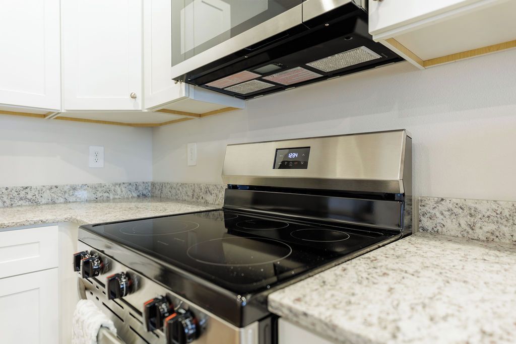 Una cocina con estufa de acero inoxidable, un reloj digital y encimeras de granito.