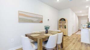 Un comedor con una mesa de madera, sillas blancas tapizadas y un florero con una planta.