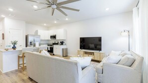 Un espacio habitable moderno con ventilador de techo, una zona de cocina, un televisor de pantalla plana y un sofá.