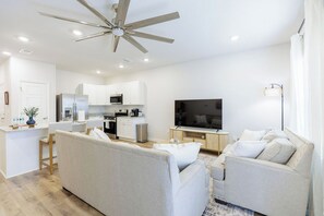 Um espaço de estar moderno, com ventilador de teto, cozinha, TV de tela plana e sofá.