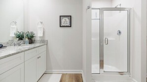 Un baño moderno con cabina de ducha de vidrio, tocador con encimera de mármol y una cita enmarcada en la pared.
