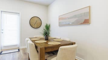 Een eetgedeelte met een houten tafel, zes stoelen, een klok, een potplant en een ingelijste foto aan de muur.