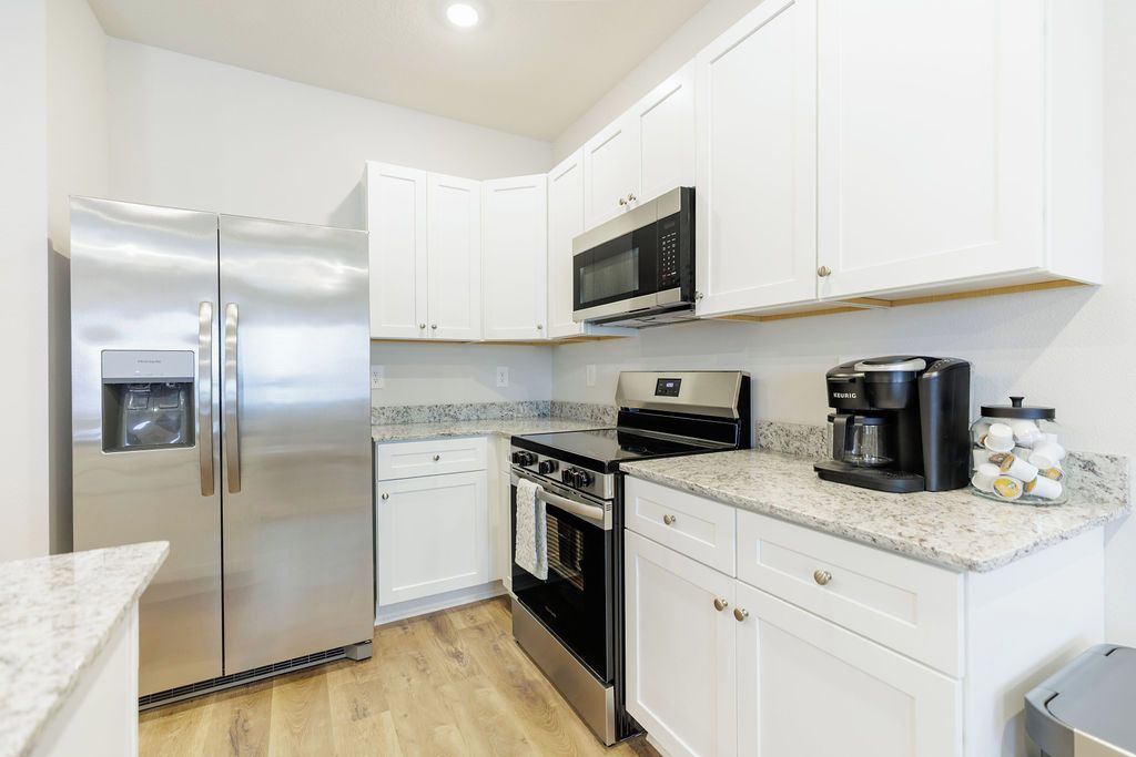 A compact kitchen with white cabinets, stainless steel appliances, a built-in microwave, a coffee maker, and a water dispenser.