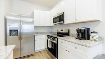 A compact kitchen with white cabinets, stainless steel appliances, a built-in microwave, a coffee maker, and a water dispenser.