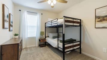 A bunk bed room with a ceiling fan, a bedside table with a lamp, and a window with curtains.