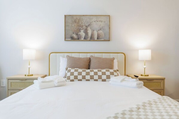 A neatly made bed with checkered pillows, two bedside lamps, and a framed artwork above.