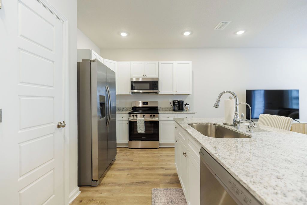A modern kitchen with stainless steel appliances, white cabinetry, and a granite countertop.