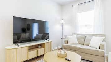 A living room with a flat-screen TV, a round coffee table, a sofa, and a floor lamp.