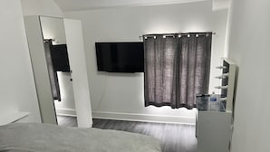 A bedroom with a bed, a TV mounted on the wall, a mirror, and a dresser.