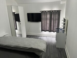 A bedroom with a bed, a TV mounted on the wall, a mirror, and a dresser.