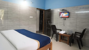 A hotel room with a bed, a TV mounted on the wall, a small table with chairs, and a shower area. - Hotel Royal Plaza (New Delhi)