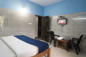 Hotellihuone, jossa on sänky, seinälle asennettu televisio, pieni pöytä tuoleineen sekä suihkutila.