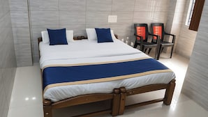 A neatly made bed with a blue and white bedspread, wooden headboard, and two bedside tables with red chairs. - Hotel Royal Plaza (New Delhi)