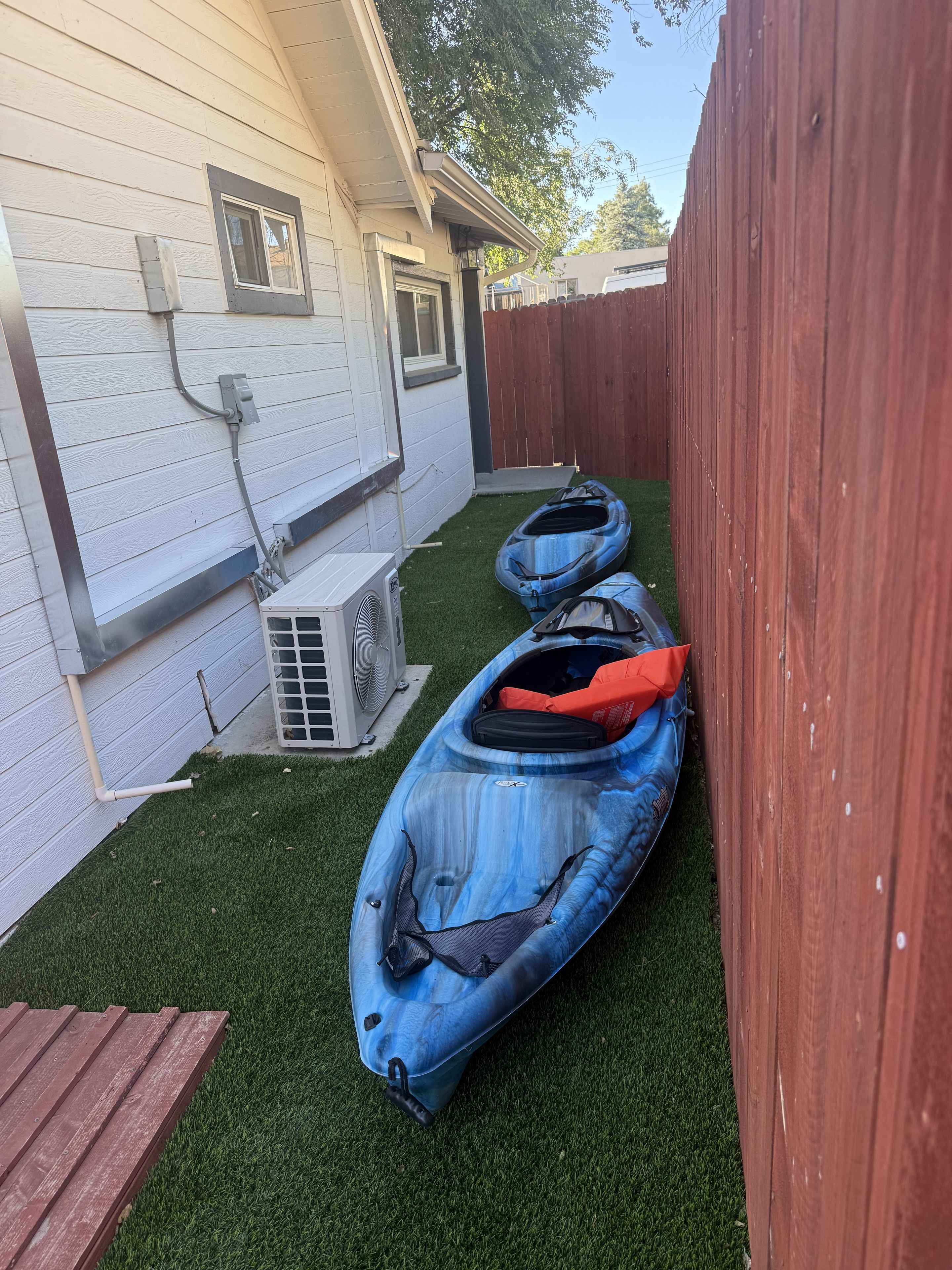 A backyard with two kayaks, a wooden deck, and a white house.