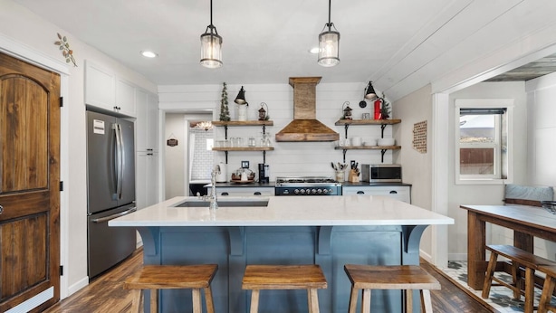 Una cocina con isla central, taburetes de madera, un refrigerador de acero inoxidable e iluminación colgante.