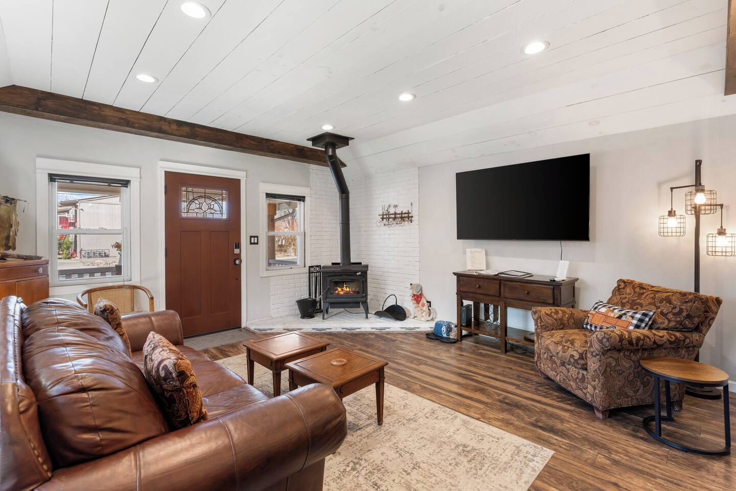 A living room with a fireplace, leather sofa, patterned armchair, and a flat-screen TV.
