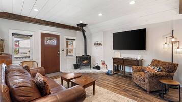A living room with a fireplace, leather sofa, patterned armchair, and a flat-screen TV.