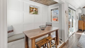 Un comedor con mesa y banco de madera, un cuadro enmarcado en la pared y una ventana con vistas al exterior.