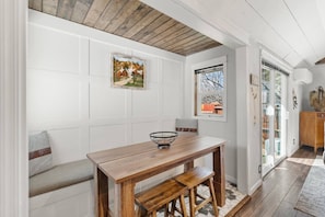 Un comedor con mesa y banco de madera, un cuadro enmarcado en la pared y una ventana con vistas al exterior.