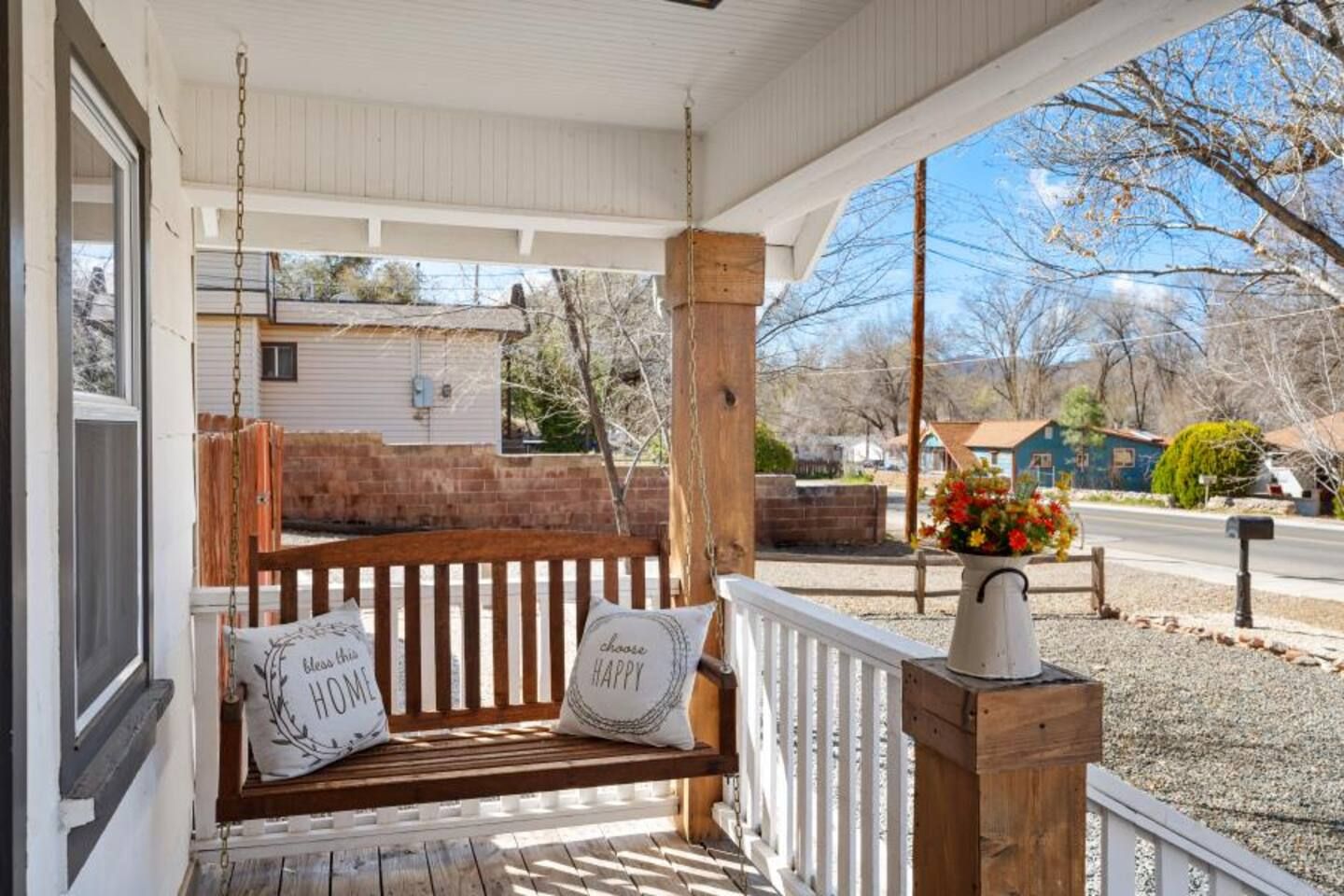 A porch with a wooden bench and two pillows, a white railing, and a flower pot.