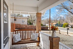A porch with a wooden bench and two pillows, a white railing, and a flower pot.