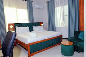 Ein Hotelzimmer mit einem Bett, einem Sessel, einem runden Hocker und einer Wandklimaanlage.