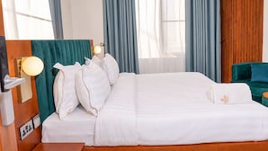 A hotel room with a large bed, a wooden headboard, a green upholstered chair, and a wooden side table. - Amani Residence Entebbe (Entebbe)