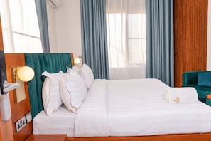 Ein Hotelzimmer mit einem großen Bett, einem hölzernen Kopfteil, einem grünen Polsterstuhl und einem Nachttisch aus Holz.